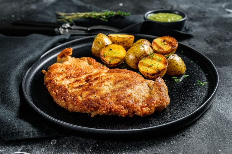 Breaded german weiner schnitzel with potatoes. Black background. Top view